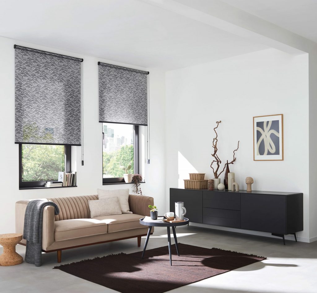 2 glatte Rollos in grau Farbtönen vor Fenstern in einem modernen Wohnzimmer mit Sofa, Sideboard und Couchtisch