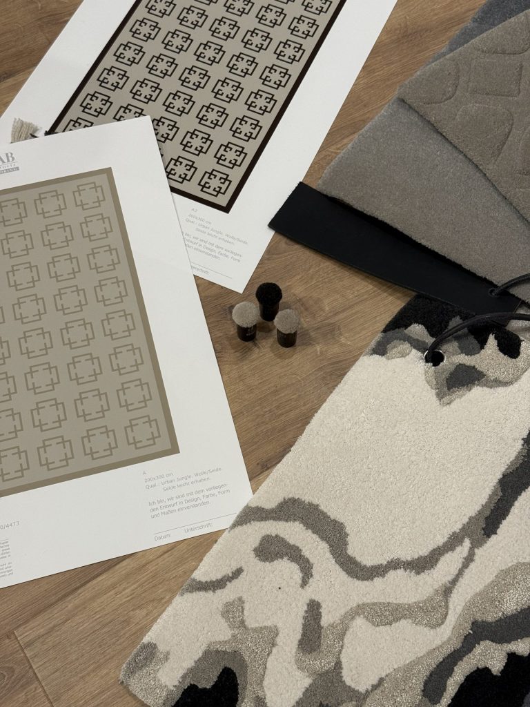 Teppichmuster, Entwurfszeichnungen und Materialproben liegen auf einem Holzboden ausgebreitet