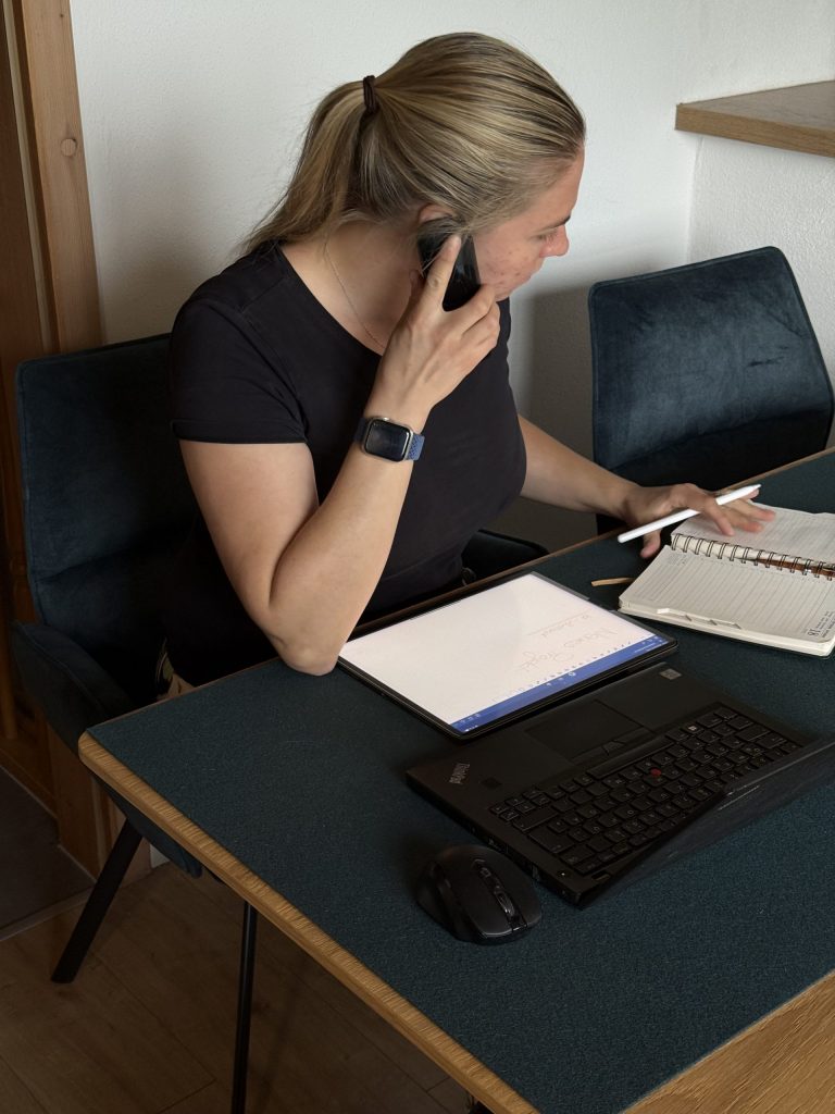 Raumausstatterin sitzt am Schreibtisch, telefoniert und macht sich Notizen auf Tablet und Papier