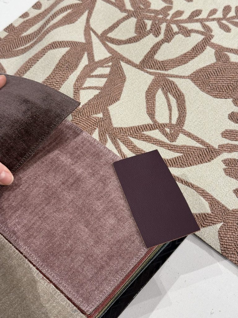 Hand hält verschiedene Stoffe und Lederproben auf einem gemusterten Stoff