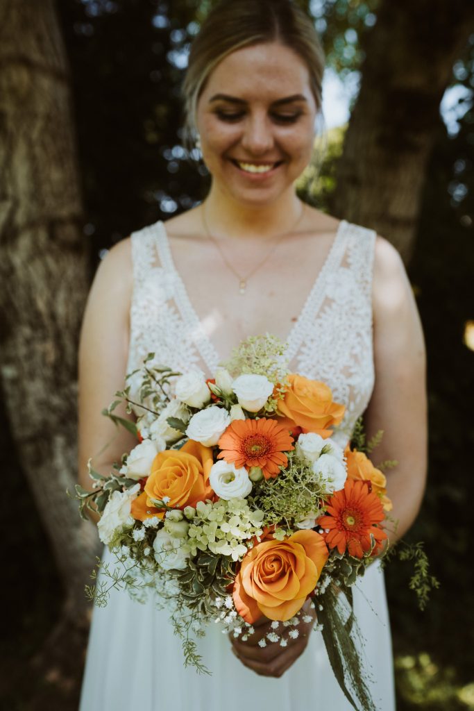 Stephanie Fürst in hellem Kleid hält einen Strauß aus weißen und orangefarbenen Blumen im Freien