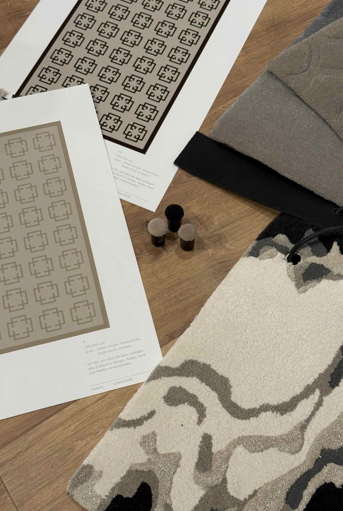 Teppichmuster, Entwurfszeichnungen und Materialproben liegen auf einem Holzboden ausgebreitet