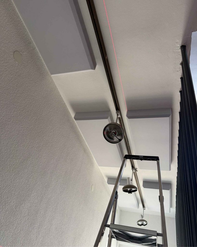 Montage von Akustikpaneelen an der Decke mit Laser und Leiter für präzise Positionierung im Hausflur