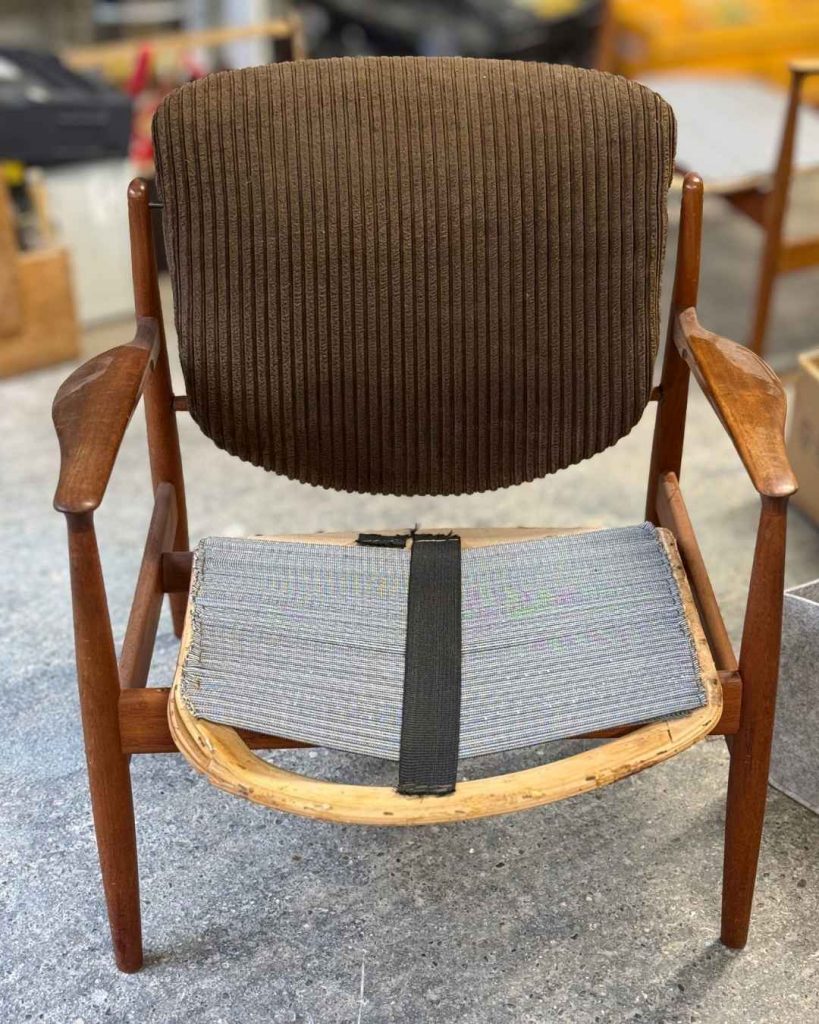 Finn Juhl 136 Sessel mit altem braunen Cordbezug auf der Rückenlehne und zerfallener Sitzfläche mit Flächengurt, Zustand bei Anlieferung in der Werkstatt