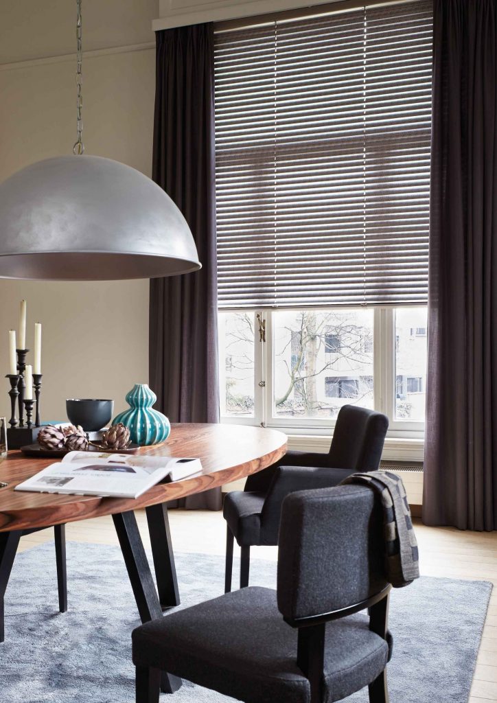 Klassisch-elegantes Esszimmer mit grauer Jalousie am Fenster, runder Holztisch und dunkle Stühle, Hängeleuchte aus Metall