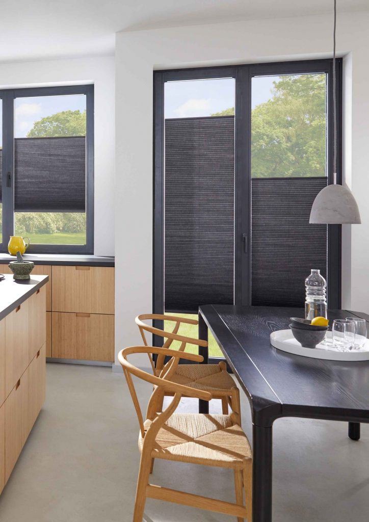 Moderne Küche mit dunklen Fensterrahmen und schwarzen Plissees zur Verdunkelung, Holztisch mit Stühlen im Vordergrund