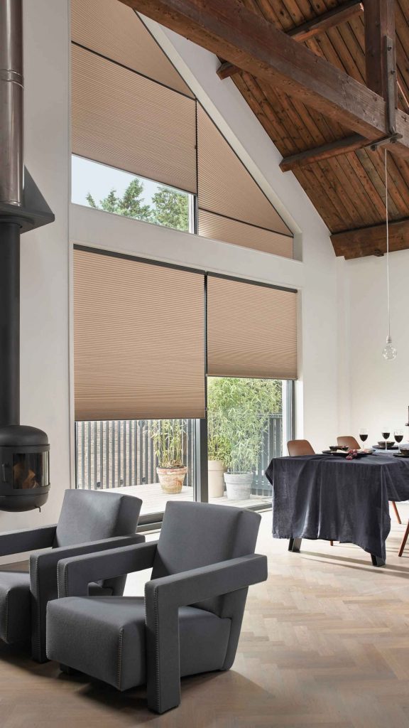 Heller Wohnraum mit hoher Decke und Holzbalken, bodentiefe Fenster und Dachschrägenfenster mit maßgefertigten Plissees in Beige