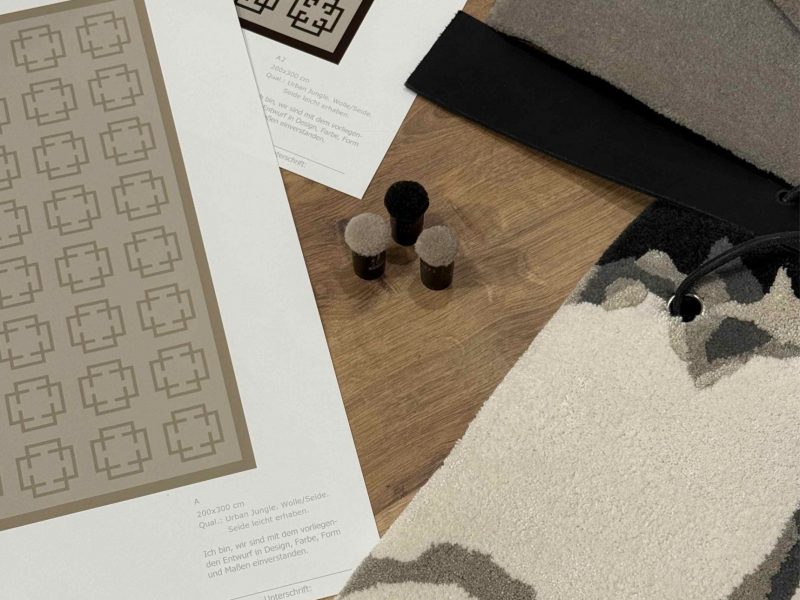 Teppichmuster, Entwurfszeichnungen und Materialproben liegen auf einem Holzboden ausgebreitet