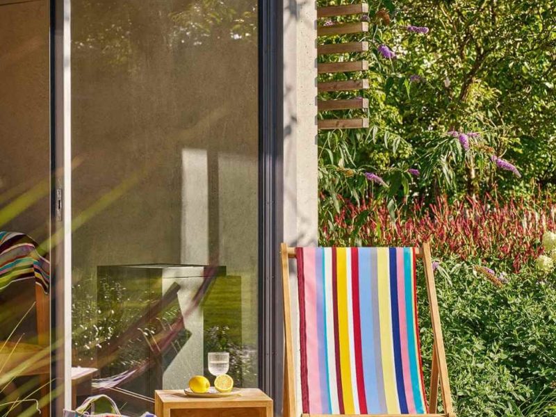 Bunter Weishäupl Liegestuhl mit Streifenbezug auf einer Terrasse zwischen Pflanzen und Gartentür