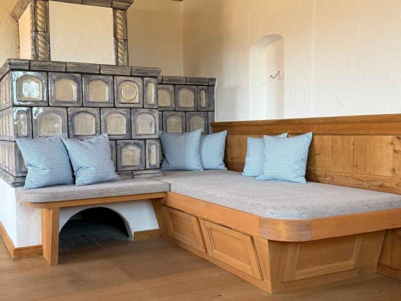Eckbank aus Holz mit maßgefertigten hellen Sitzpolstern und gemusterten Kissen