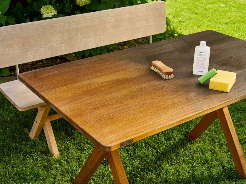 Weishäupl Gartentisch aus Teakholz mit Pflegemitteln und Bürste auf grünem Rasen