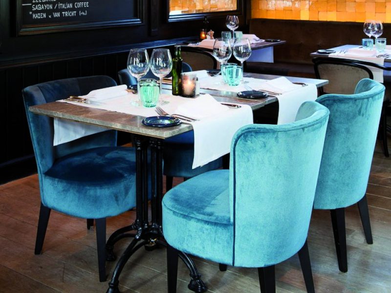 Mehrere Stühle Marty aus der DMG Kollektion, mit blauem Samt bezogen, arrangiert in edlem Ambiente – erinnert an ein nobles Restaurant.