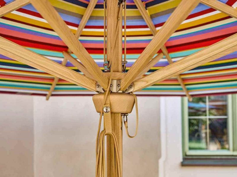 Blick von unten in einen aufgespannten Weishäupl Professional Sonnenschirm mit buntem Multicolor-Bezug und Holzstreben