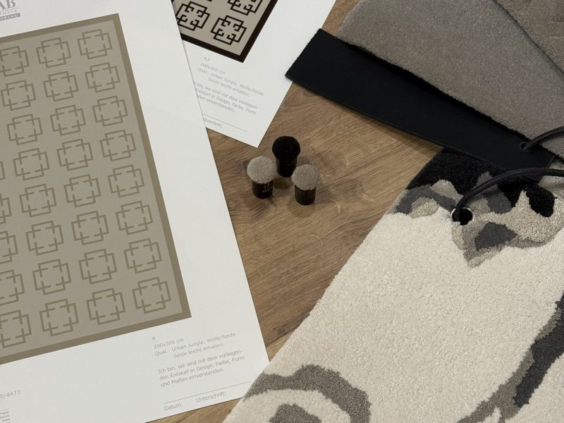 Teppichmuster, Entwurfszeichnungen und Materialproben liegen auf einem Holzboden ausgebreitet