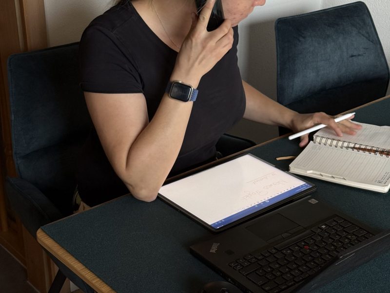 Raumausstatterin sitzt am Schreibtisch, telefoniert und macht sich Notizen auf Tablet und Papier