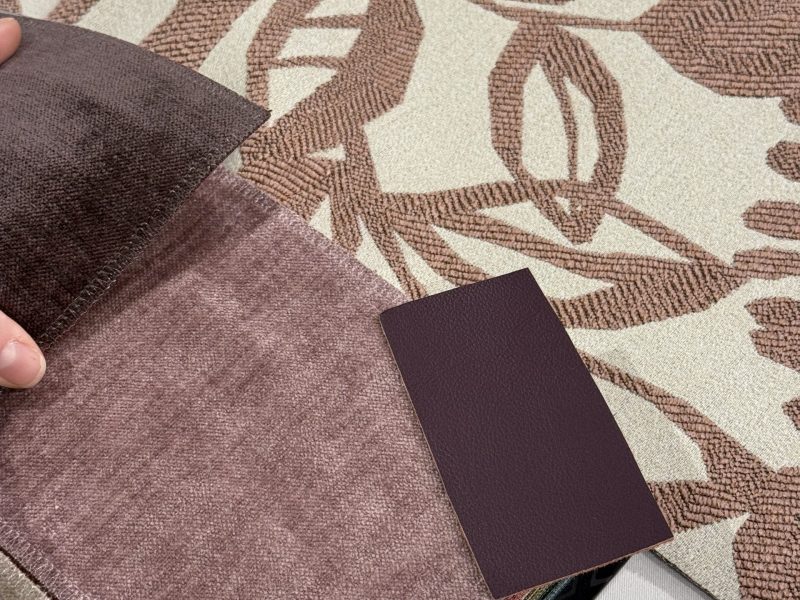 Hand hält verschiedene Stoffe und Lederproben auf einem gemusterten Stoff