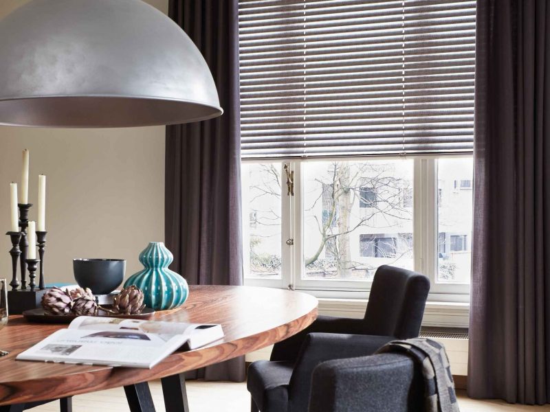 Klassisch-elegantes Esszimmer mit grauer Jalousie am Fenster, runder Holztisch und dunkle Stühle, Hängeleuchte aus Metall