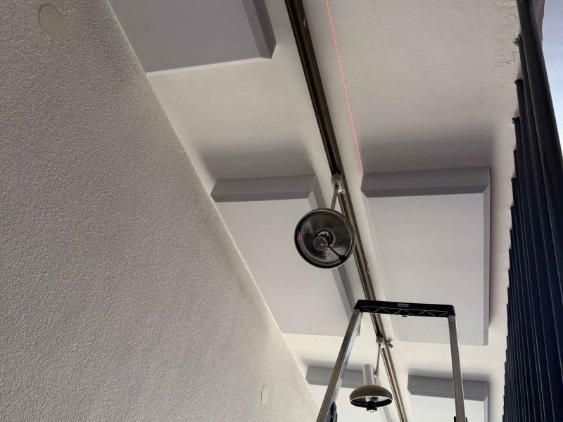 Montage von Akustikpaneelen an der Decke mit Laser und Leiter für präzise Positionierung im Hausflur