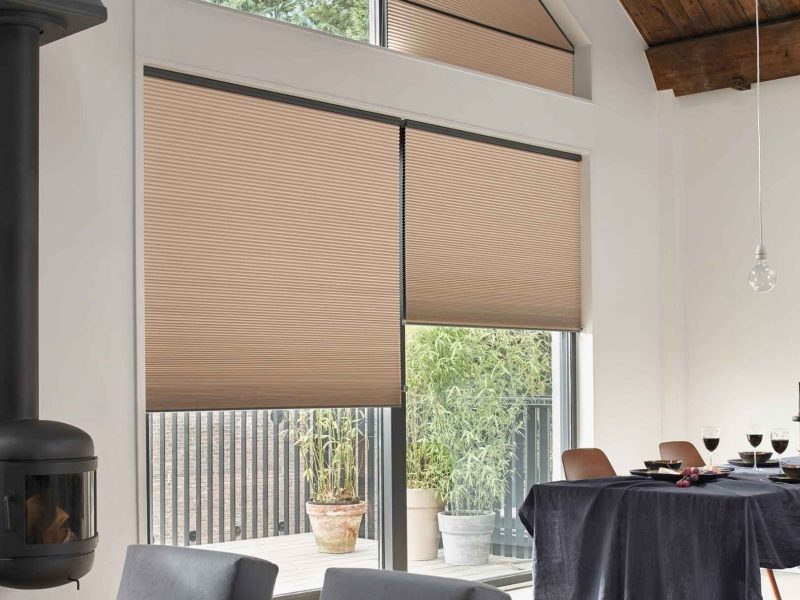 Heller Wohnraum mit hoher Decke und Holzbalken, bodentiefe Fenster und Dachschrägenfenster mit maßgefertigten Plissees in Beige