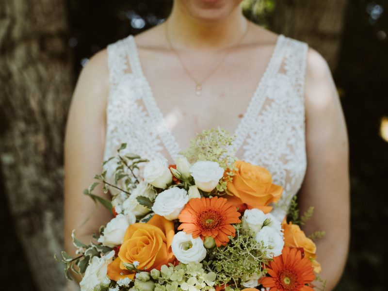 Stephanie Fürst in hellem Kleid hält einen Strauß aus weißen und orangefarbenen Blumen im Freien